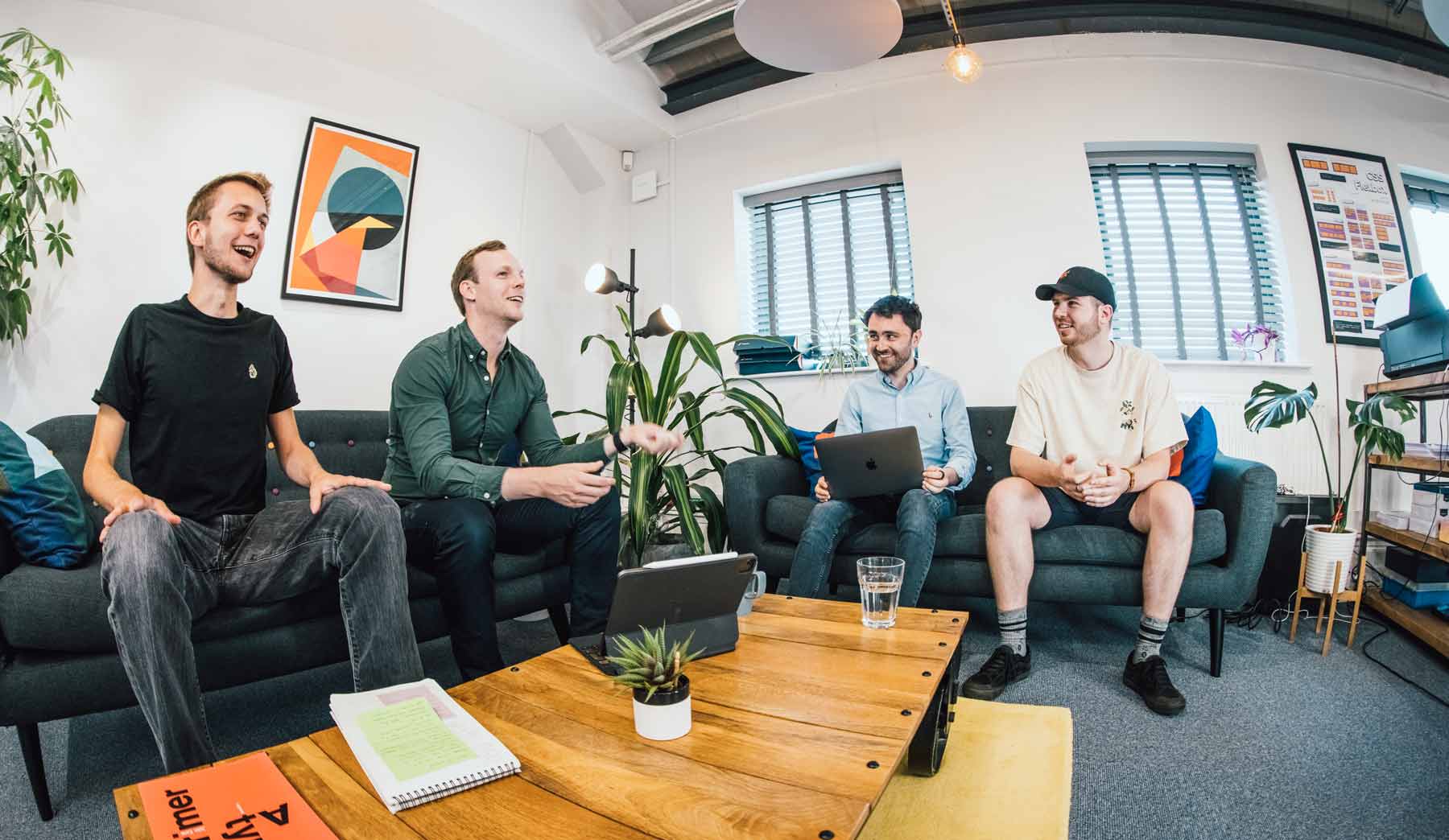 Photo of 4 of the mmtm team chatting and laughing on the sofas in the office